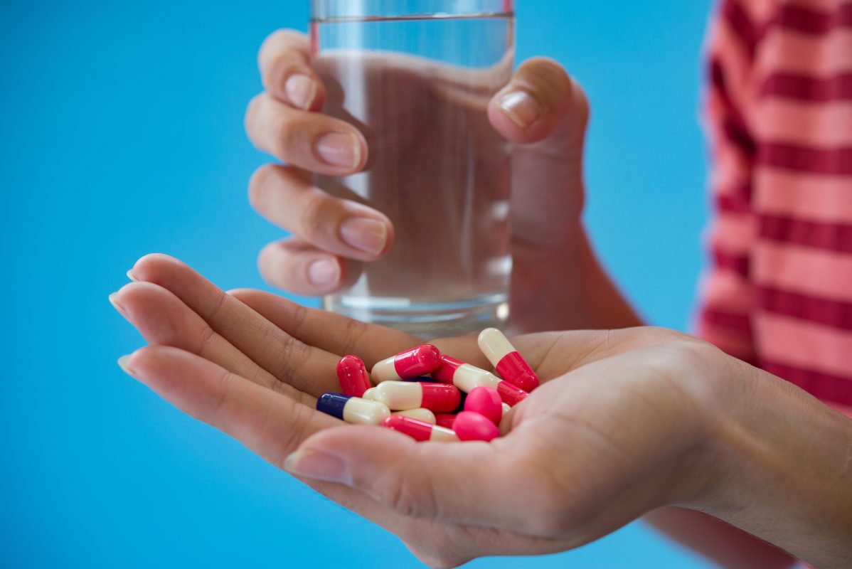 person holding a glass of water in one hand, supplements in the other hand