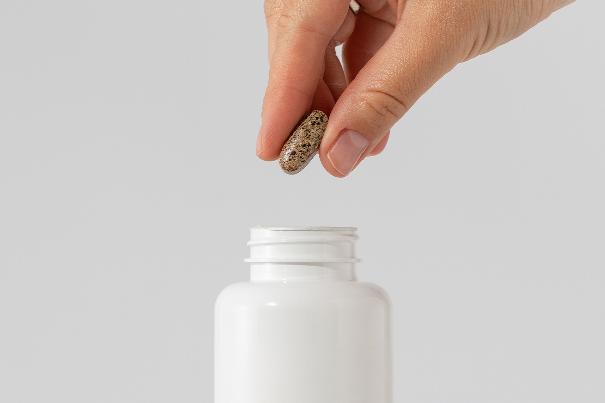 white supplement bottle person holding a piece of capsule 