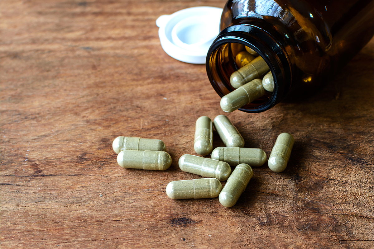 light green capsules on wooden table and amber glass bottle