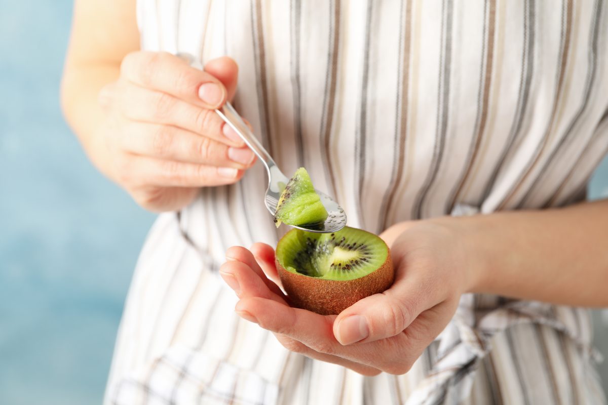 woman holding spoon and kiwi