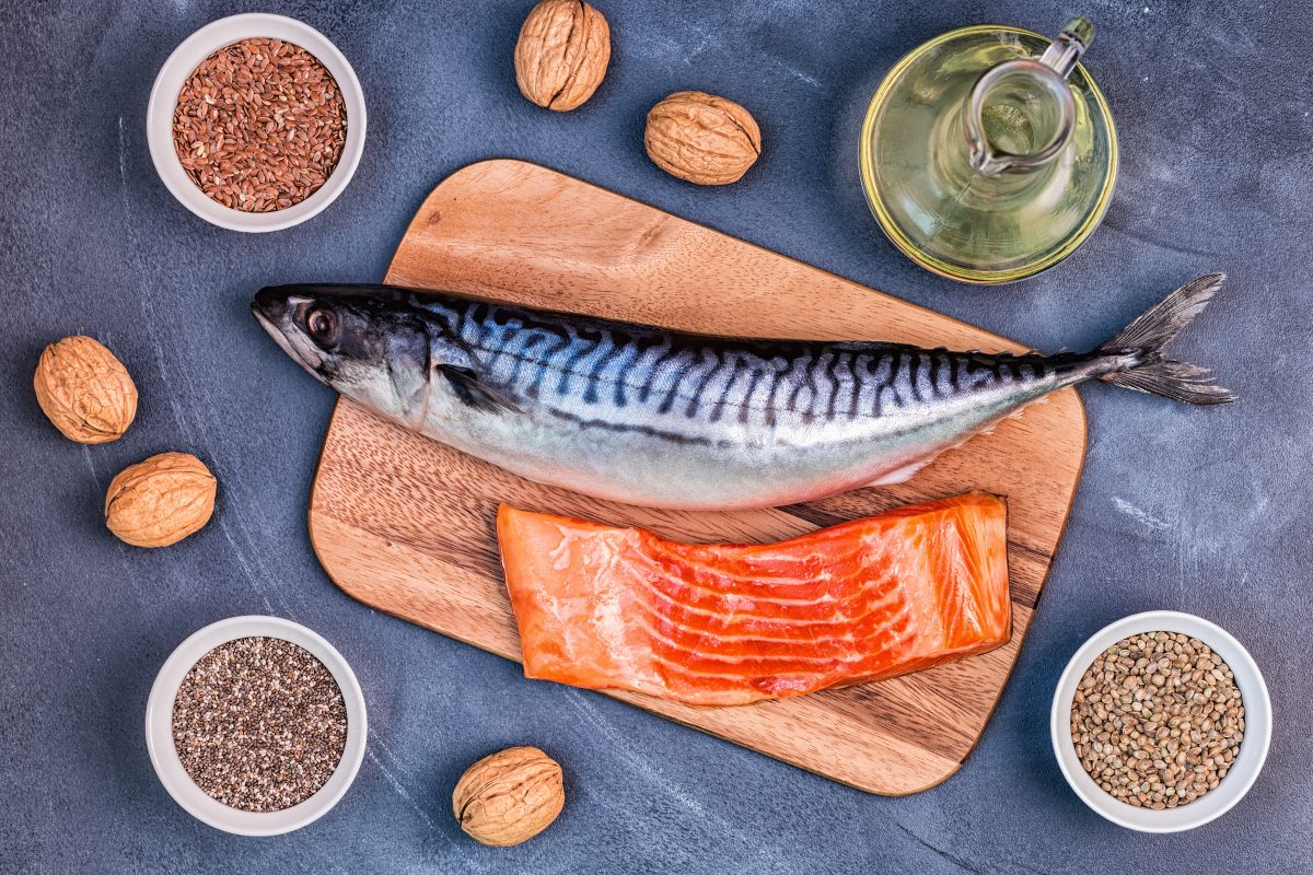 salmon on wooden chopping board surrounded by chia seeds, flaxseeds, walnuts in white bowl