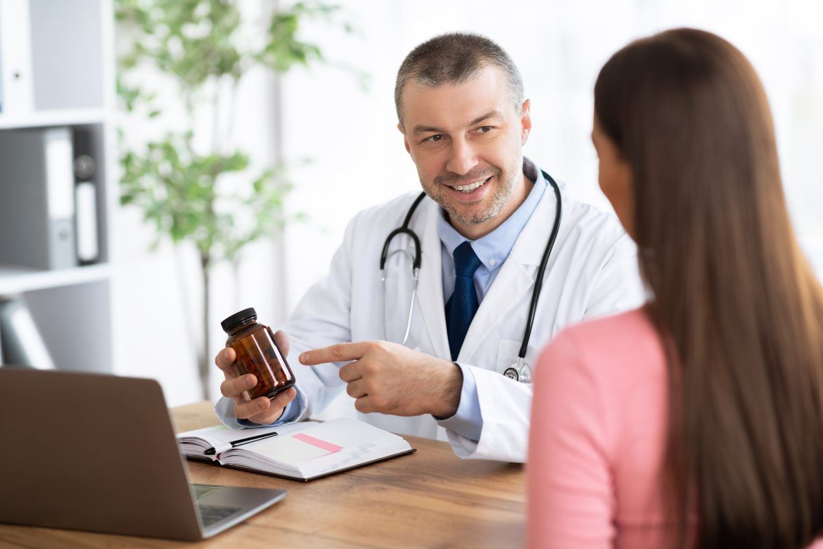 male doctor holding a supplement bottle speaking with a woman patient