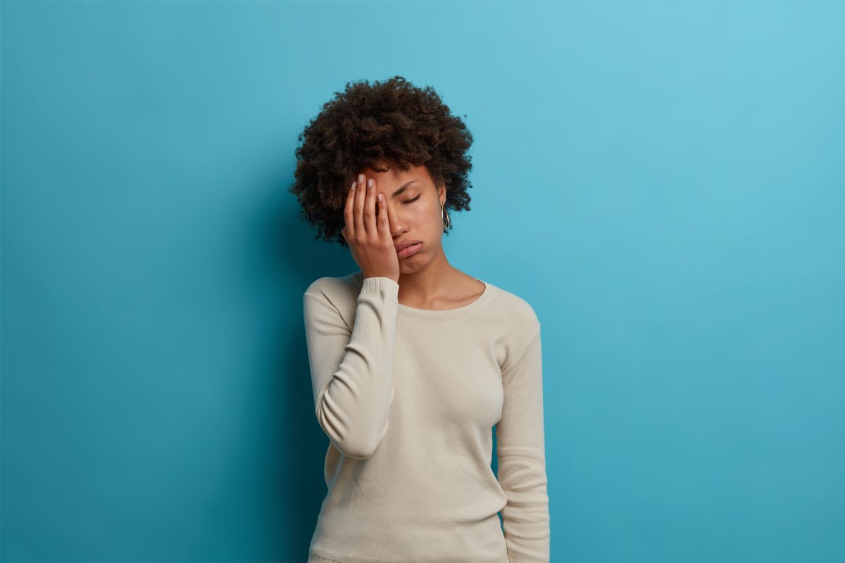 woman standing in front of blue wall looking tired
