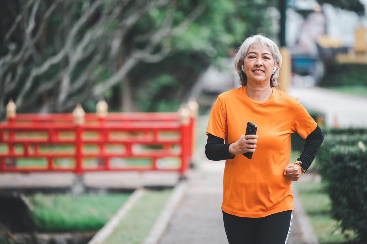 woman wearing orange shirt running outdoors holding smartphone